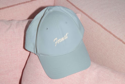 Baseball cap with embroidered font logo resting on a pink fabric background cap mockup for branding design template neutral colors for designers