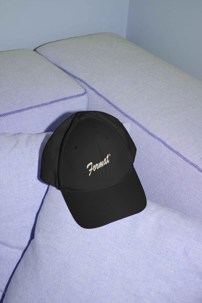 Black baseball cap on light purple sofa displaying curved text mockup design suitable for branding apparel fashion accessories for designers