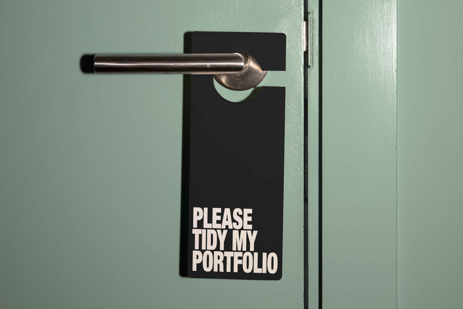 Black blank door tag hanging on brushed steel handle against mint green door