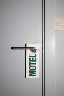 Door hanger tag in teal on chrome handle against white hotel room wall