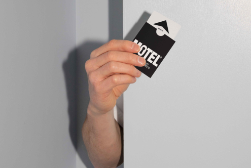 Hand holding black card with white HOTEL text against white wall