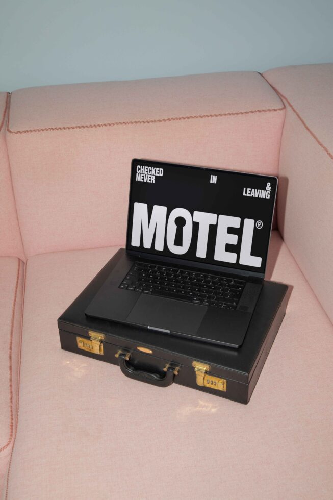 Laptop mockup on a pink sofa with a vintage briefcase digital screen displaying bold motel-themed graphic design keywords mockups templates designers.