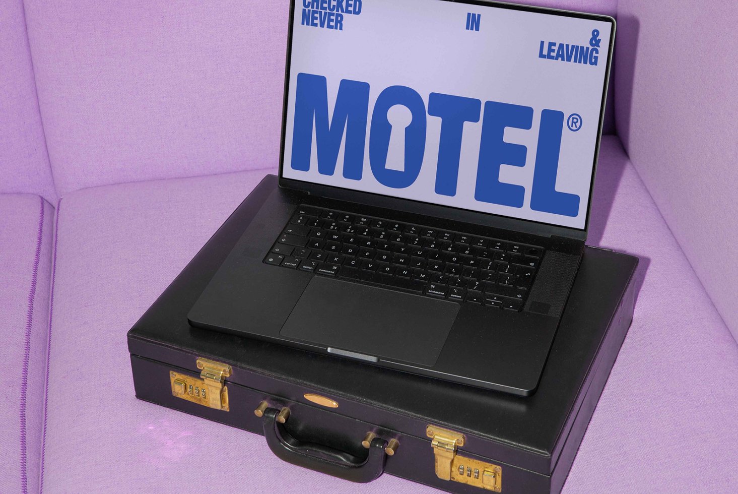 Laptop on suitcase with MOTEL graphic on screen, placed on a purple sofa. Ideal for mockup templates, graphic design assets, digital creatives.
