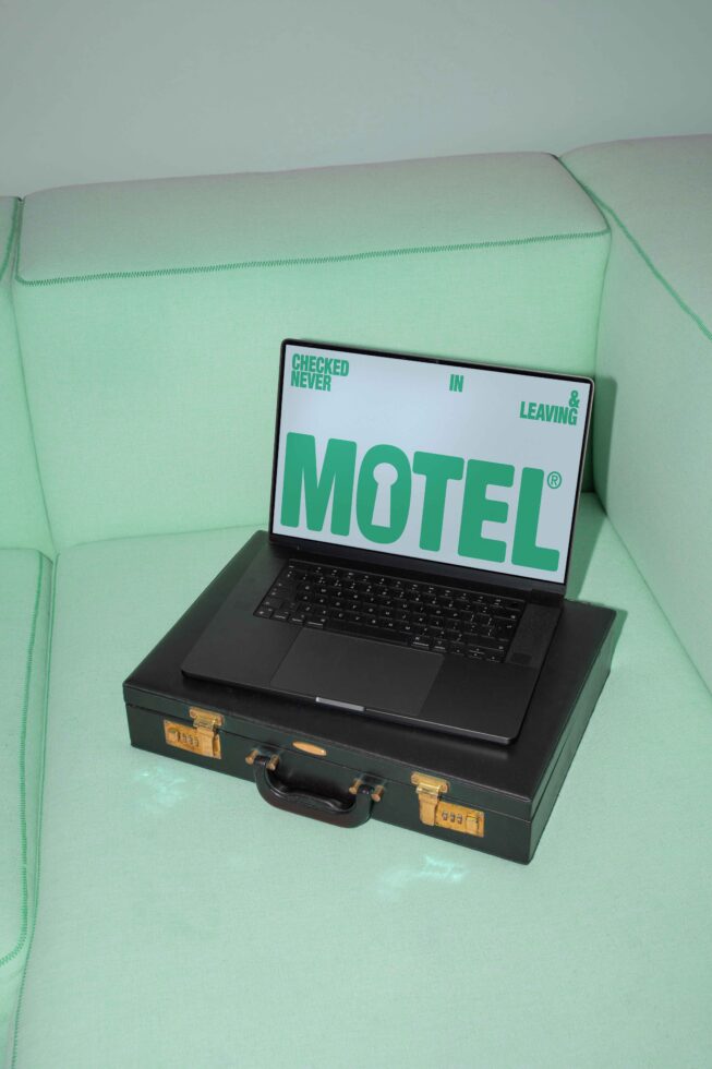 Laptop on vintage suitcase displaying motel-themed graphic design on mint green sofa SEO keywords: mockup design graphic template creative asset