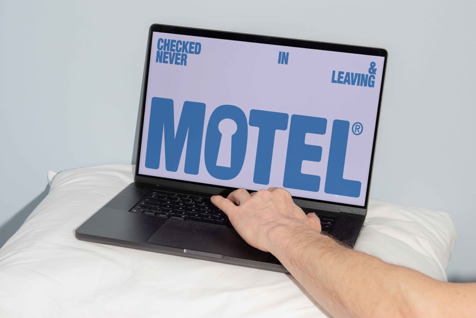 Laptop on bed showing motel sign in lilac with blue typography