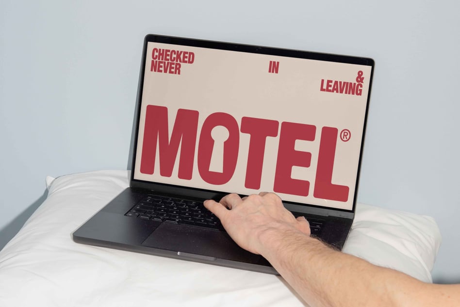 Laptop on bed with motel sign displayed in cream with burgundy text