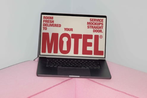 Laptop displaying bold red text on a soft pink surface, featuring digital mockup design assets for creative professionals and designers.
