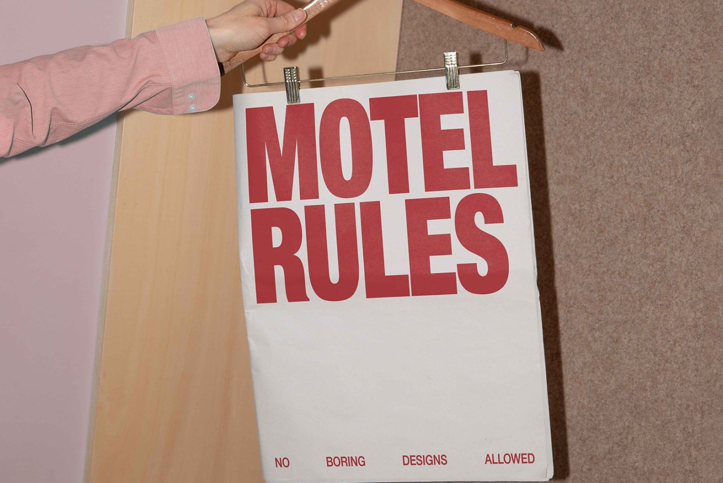 Bold red text on white paper reads Motel Rules with emphasis on typography design. Held by a person on a wooden hanger. Graphic design asset.
