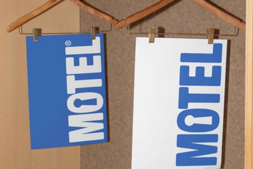 Two poster mockups with bold blue and white text reading MOTEL hanging on wooden hangers. Ideal for design presentations and showcasing branding.