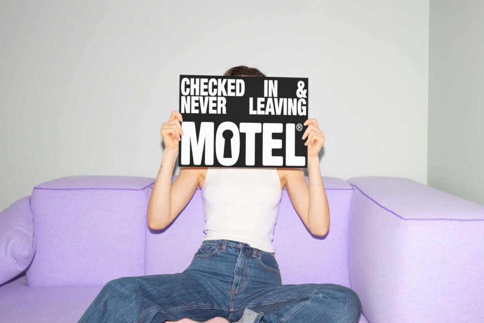 Person holding black motel sign on purple couch mockup