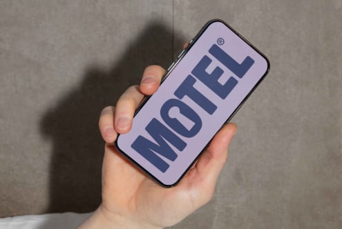 Close-up of a hand holding a smartphone displaying a bold sans-serif font spelling MOTEL on a lavender screen. Perfect for font design mockups.