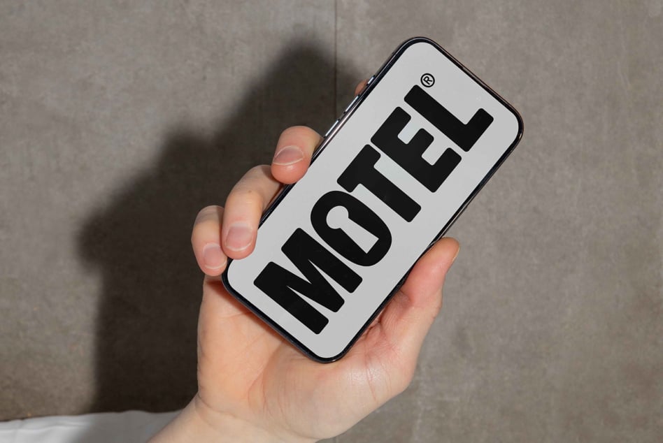 Hand holding phone with bold MOTEL text design. Ideal for templates mockups branding. Minimalist style photo. Perfect for graphic designers.