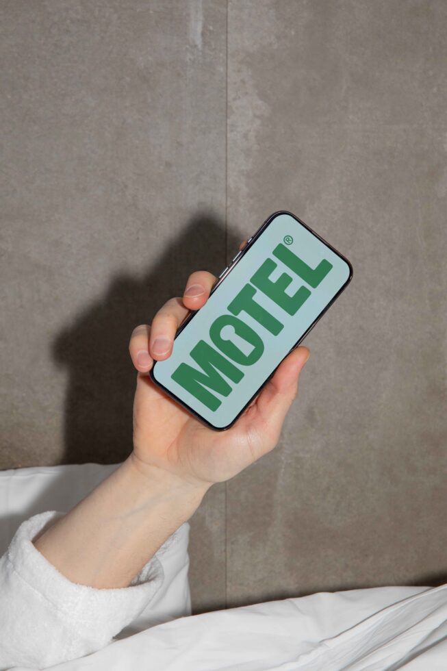 Hand holding a smartphone displaying Motel text design. Perfect for mockups, showcasing fonts, graphics, templates. Ideal for designers and creatives.