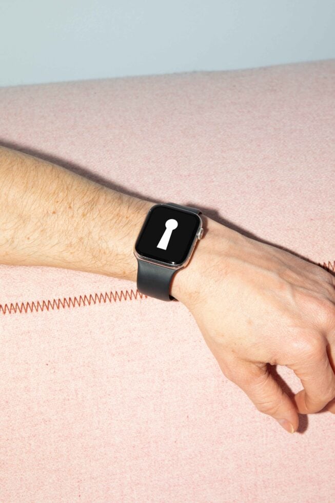 Smartwatch mockup on a wrist with black band and blank dark display featuring keyhole symbol against pink fabric background. Ideal for design presentations.
