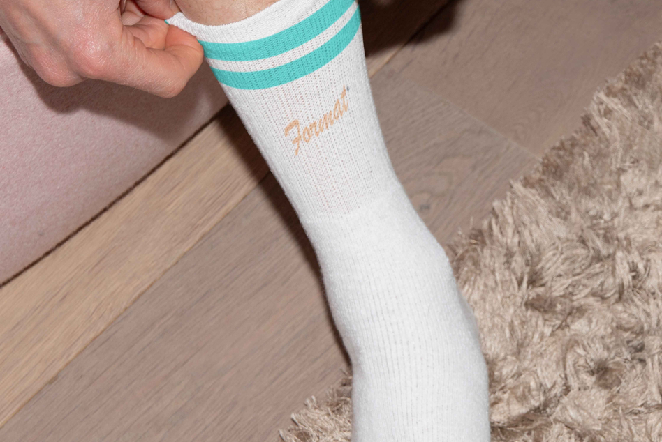 Person wearing white crew sock with teal stripes showing Format text on leg