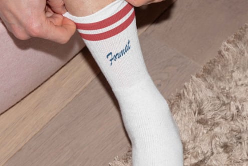 Close-up of a person adjusting a white sock with red stripes and the word Format. Ideal for fashion mockups, apparel design, and branding projects.