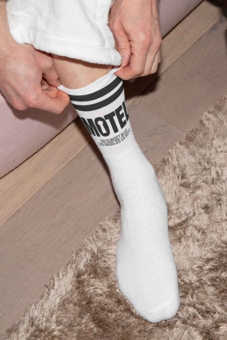 Person wearing white crew sock with black stripes showing MOTEL text on leg