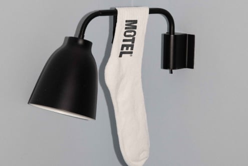 Black wall-mounted lamp with a white sock draped over it, featuring the word Motel. Ideal for designers, mockups, and interior inspiration.