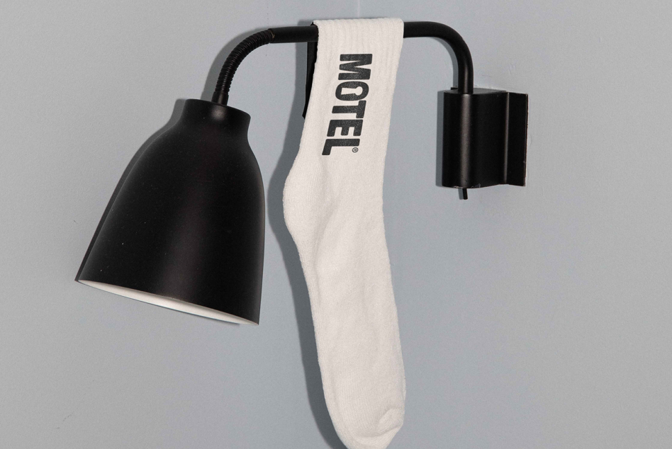 Black desk lamp with white crew sock draped over arm showing MOTEL text