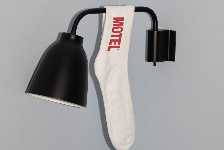 Black desk lamp with white crew sock draped over arm showing MOTEL in red