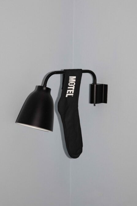 Black fabric keychain with Motel text branding on strap, metal hardware
