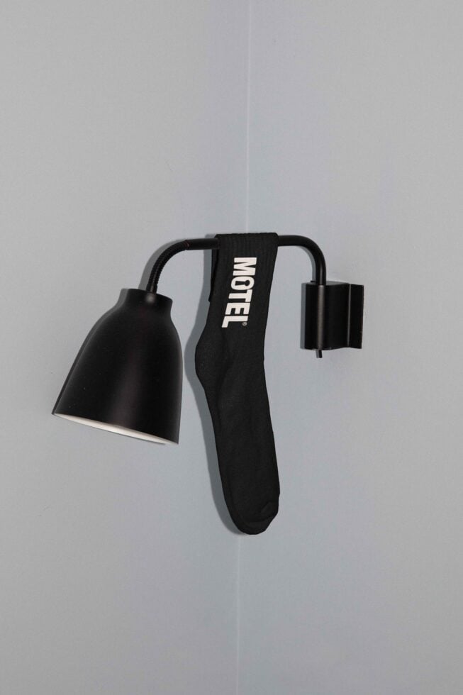 Wall-mounted black lamp with a single black sock hanging on it against a gray background. Minimalist design perfect for home decor mockups.