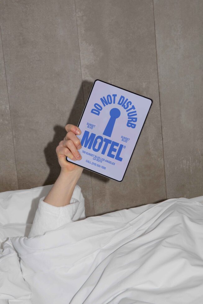 Person holding a tablet with a Do Not Disturb motel sign design in a bed setting, perfect for mockups and digital design projects, isolated background.