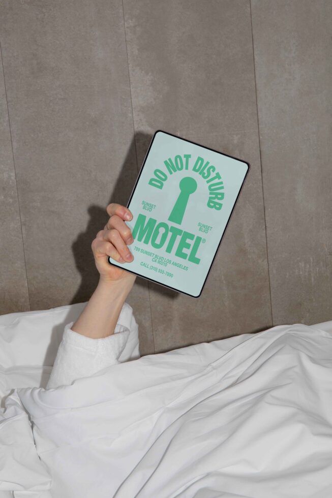Person in bed holding a tablet with a Do Not Disturb graphic displaying motel details; ideal for digital design mockups and branding inspiration.