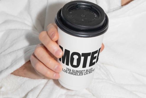 Person holding a coffee cup with bold typography design reading Motel suitable for graphics mockups templates featuring coffee branding and packaging.
