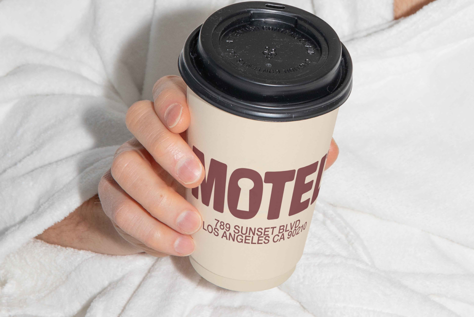 Cream cup with burgundy text held by hand on textured white sheet background