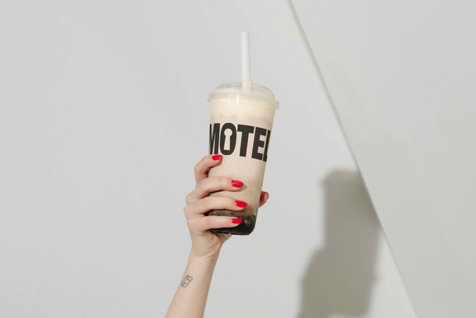 Coffee cup with black label band held by hand with red nails on white backdrop