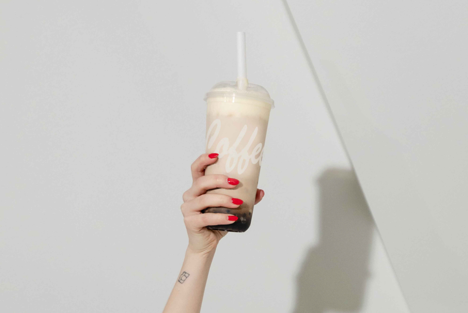 Iced boba tea with white label held by hand with red nails against white wall
