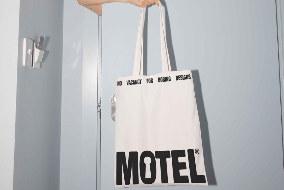 Cream tote being held showing No Vacancy for Boring Designs text, Motel logo