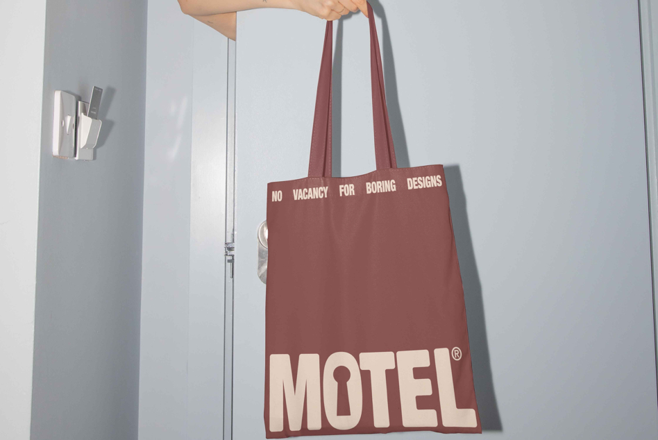 Burgundy tote on shoulder with No Vacancy for Boring Designs, Motel wordmark