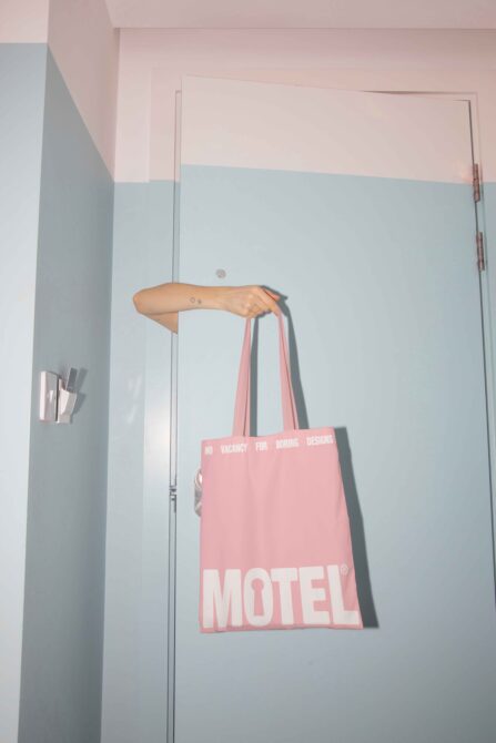 Pink tote bag on arm with No Vacancy for Boring Designs wording, Motel branding