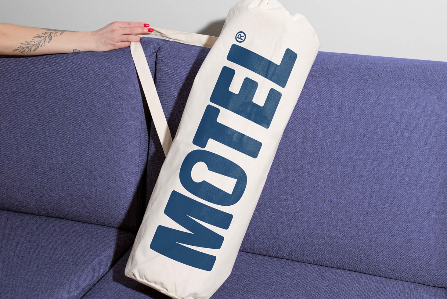 Canvas bag with bold MOTEL text against blue fabric background ideal for mockups accessories logos branding tote design templates marketplace.