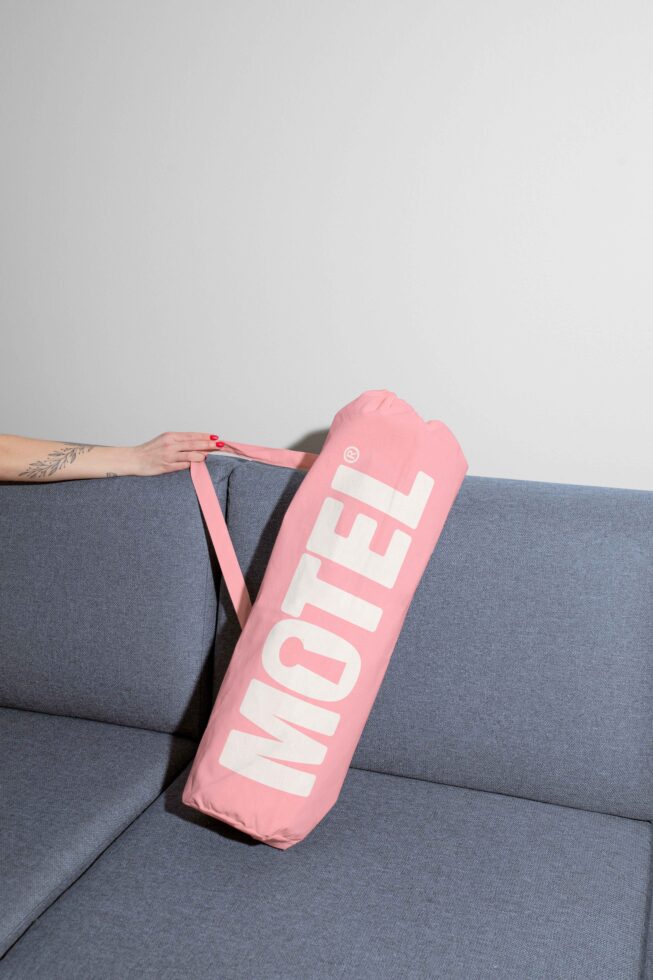 Pink bag with Motel text placed on a blue sofa background for mockup. Ideal for branding and design projects, editable for creative assets use.