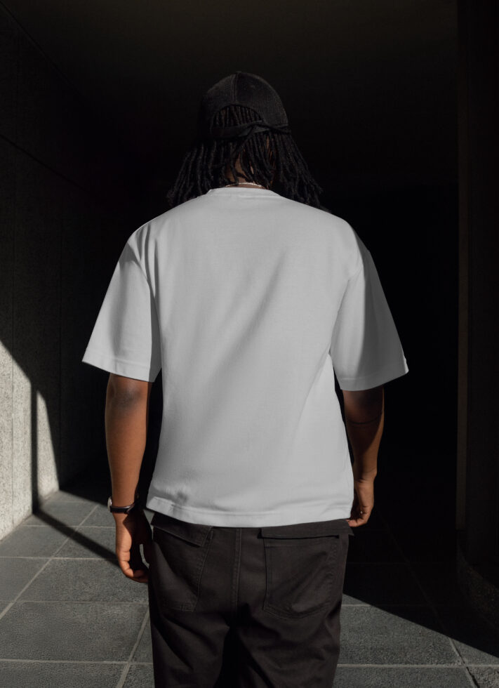 Blank white t-shirt mockup on person with dark hair and cap standing in shaded area ideal for designers and branding showcases apparel design.