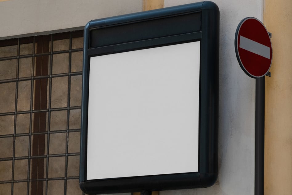 Blank tablet screen in black frame mounted on textured wall next to traffic sign
