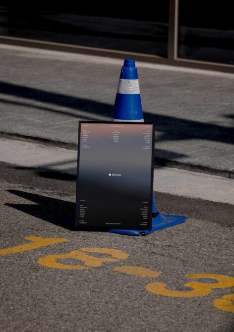 Black poster mockup propped against blue traffic cone on street with yellow markings