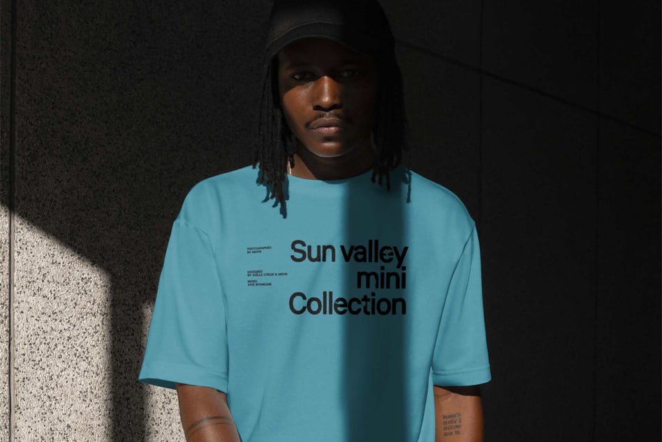 Person in light blue tee with text print standing against concrete wall