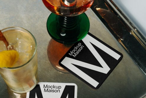 Mockup Maison coaster on a reflective table with drinks. Modern design mockup template for branding. Perfect for showcasing branding assets.