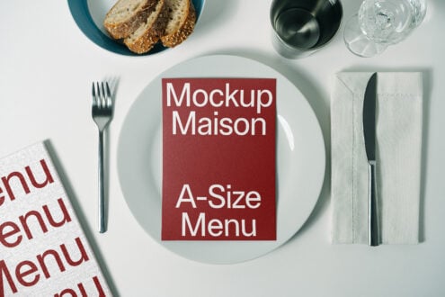 A mockup featuring a red A-size menu card on a white plate with cutlery and bread. Ideal for restaurant branding, menu design, and graphic resources.