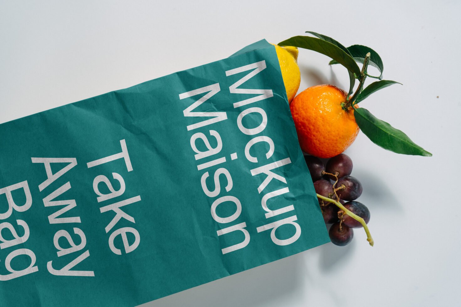 Teal paper take-away bag mockup containing citrus fruits and grapes on white background. Perfect for packaging design templates or food mockups.