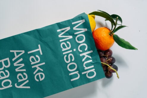 Teal paper take-away bag mockup containing citrus fruits and grapes on white background. Perfect for packaging design templates or food mockups.