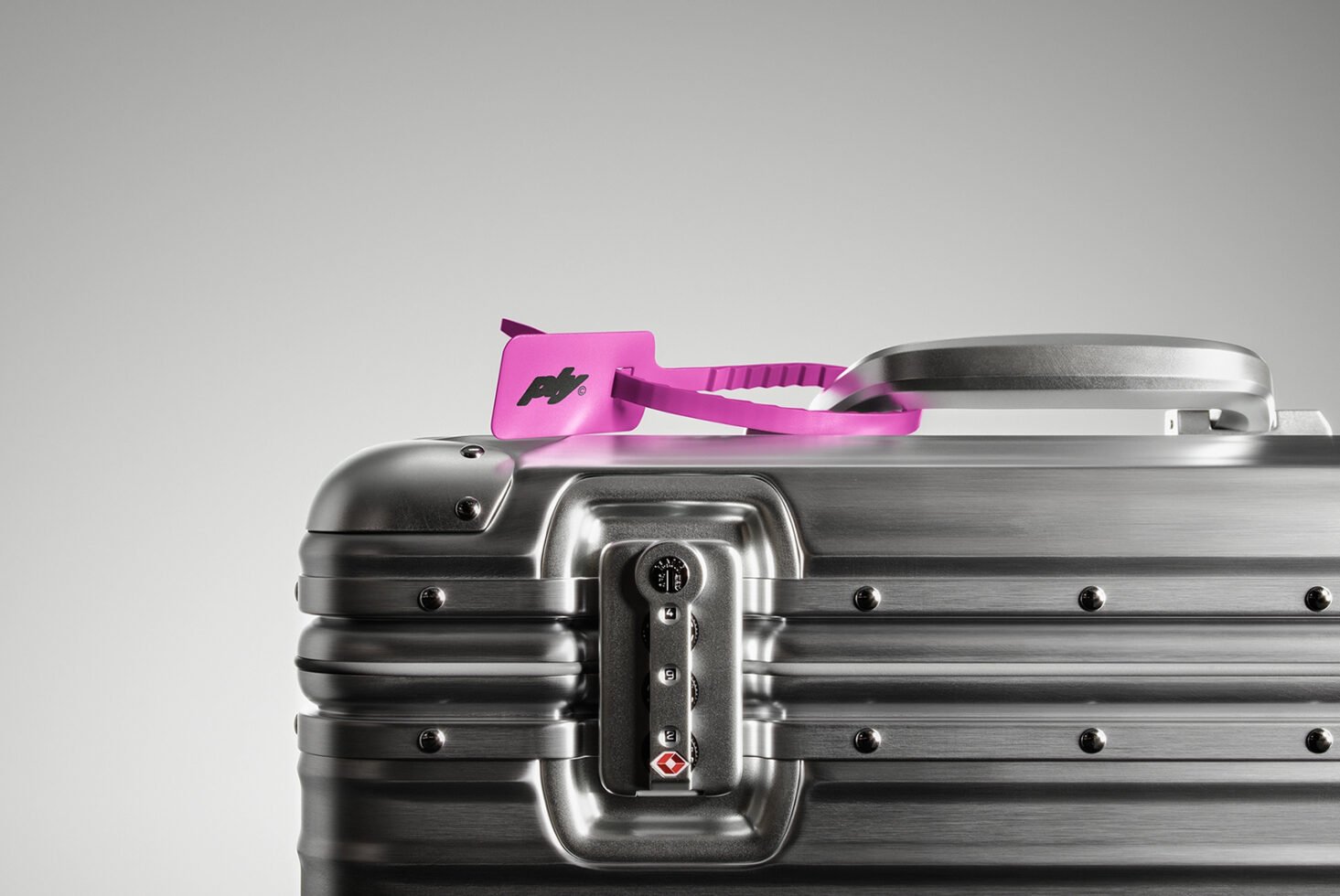 Silver metal suitcase with a pink luggage tag on top. Focus on lock and handle. Perfect for travel mockups and product design. High-quality image.