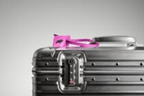 Silver hardcase luggage with bright pink TSA-approved tag attached to handle
