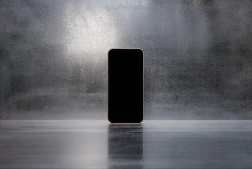 Minimalist smartphone mockup standing on reflective surface with textured gray background. Perfect for showcasing apps. Keywords: Mockup Design Template.