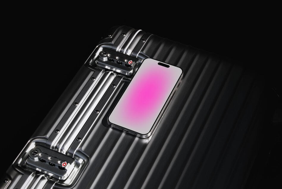 Smartphone resting on sleek metallic suitcase with pink screen display. Ideal for device mockups and technology design projects. Modern and stylish.
