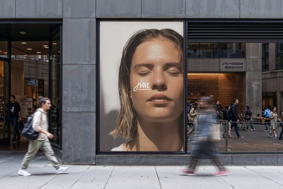 Street scene with large fashion poster of woman with eyes closed displayed on urban building exterior. Ideal for mockups, showcasing urban advertising designs.